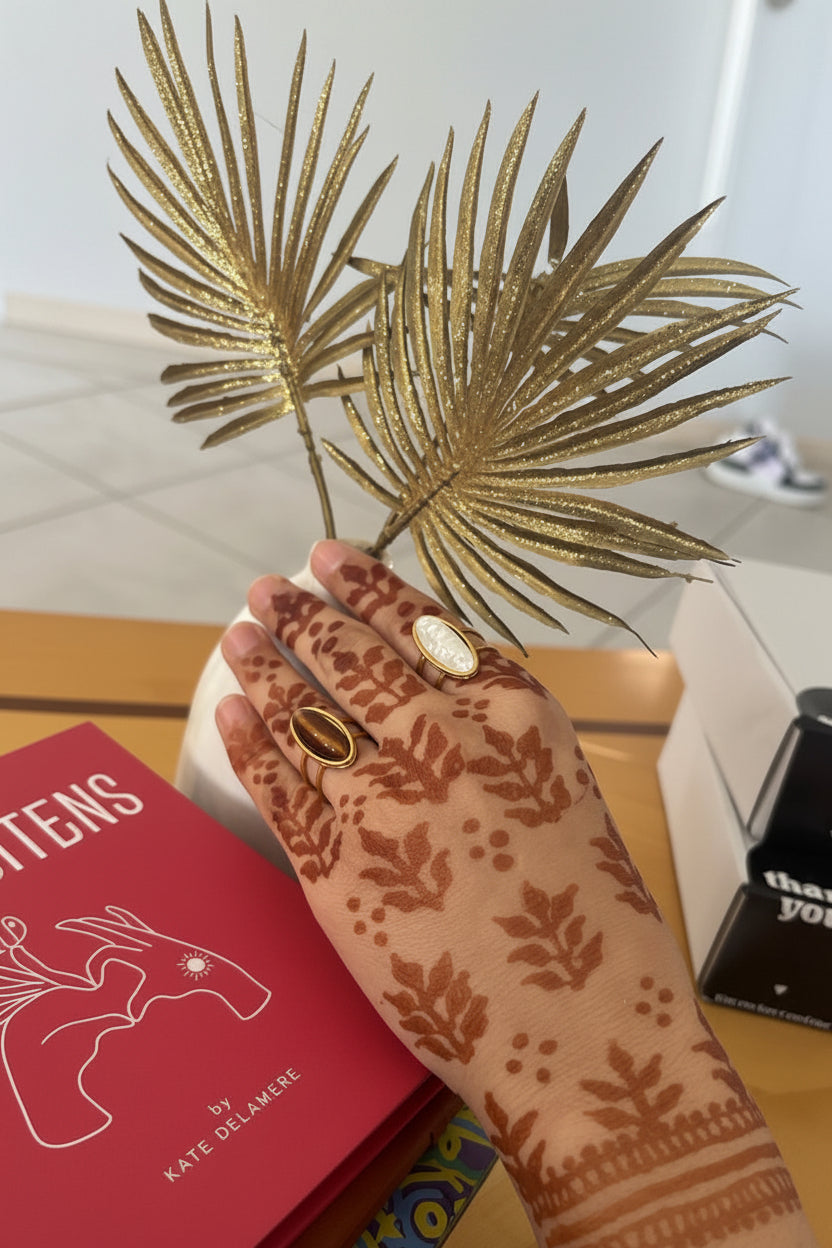 Hand with intricate henna design holding a red book titled 'Lions' by Kate Delamere.
