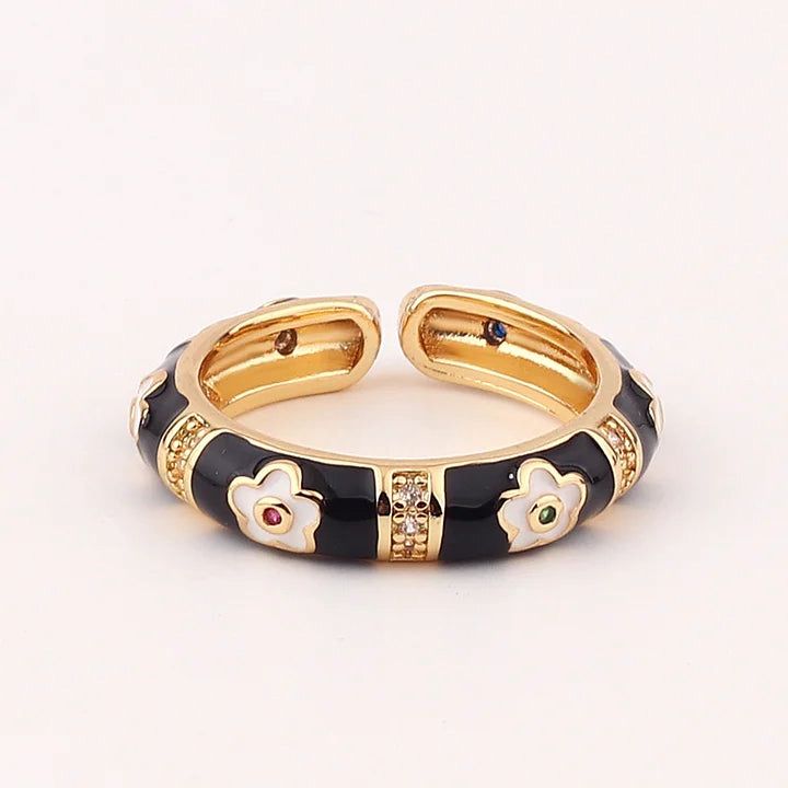 Gold and black ring with floral designs and gemstones on a white background