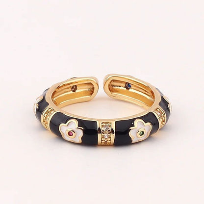 Gold and black ring with floral designs and gemstones on a white background