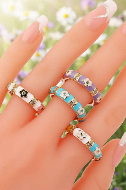 Colorful floral-patterned rings on a hand against a white background