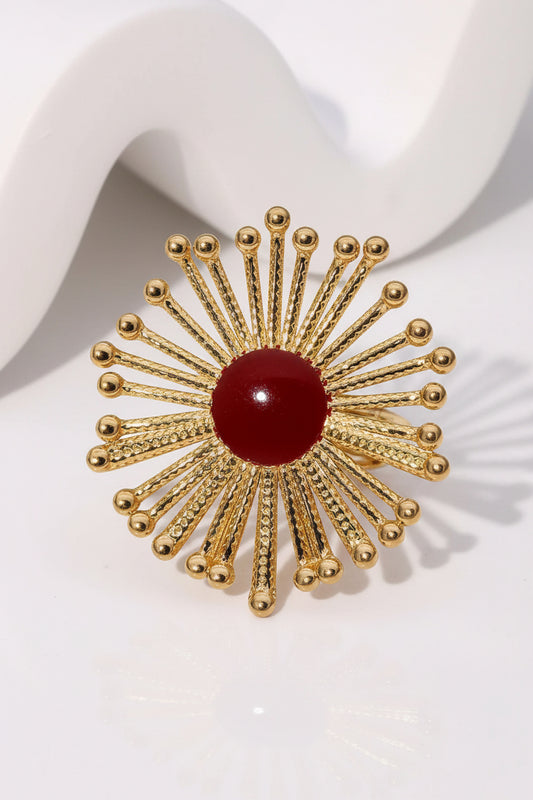 Gold plated sunburst ring with a red center on a white background
